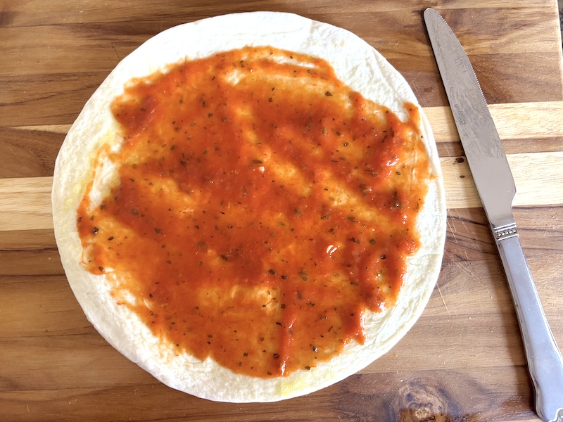 Step 1 of making these tortilla pizza is to spread the sauce on the tortilla
