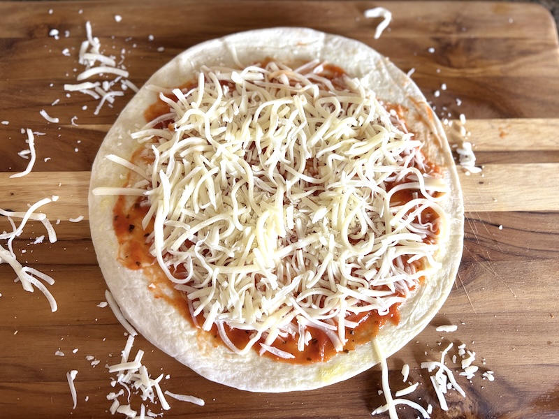 Step 2 of making the tortilla pizza is to sprinkle on the shredded cheese