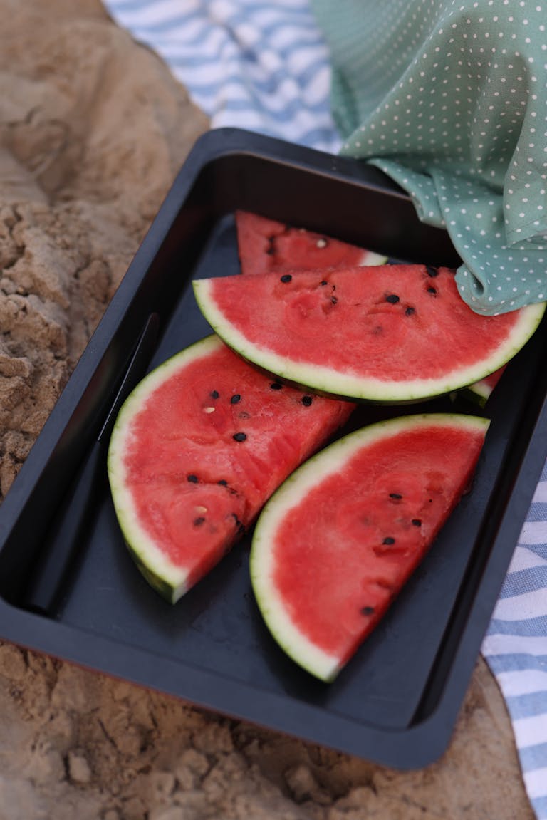 Juicy watermelon slices on a black tray outdoors, perfect for summer picnics.