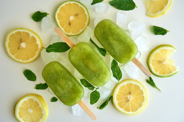 Top view of green ice pops with lemon slices and mint leaves on ice. Perfect for summer.