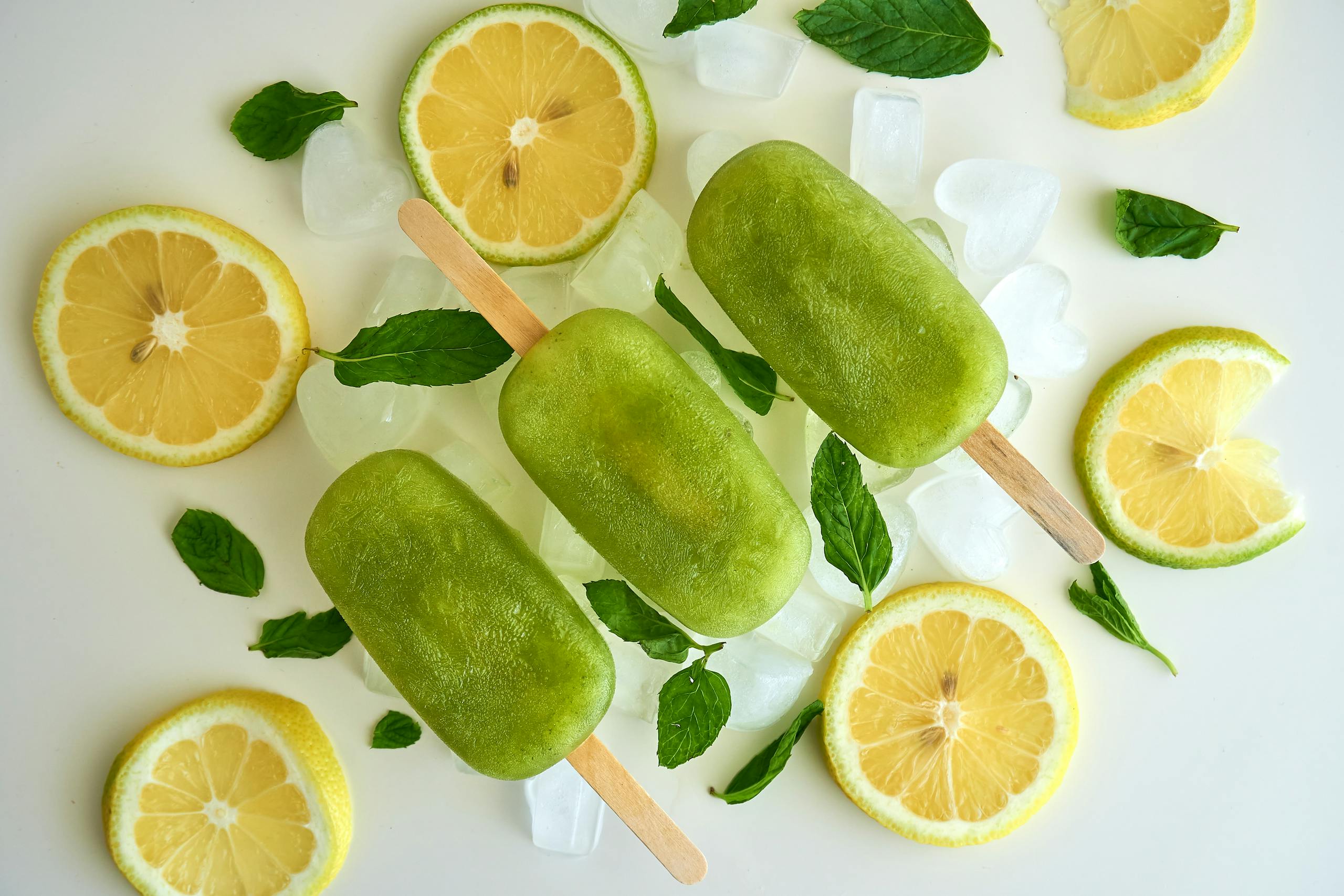 Top view of green ice pops with lemon slices and mint leaves on ice. Perfect for summer.