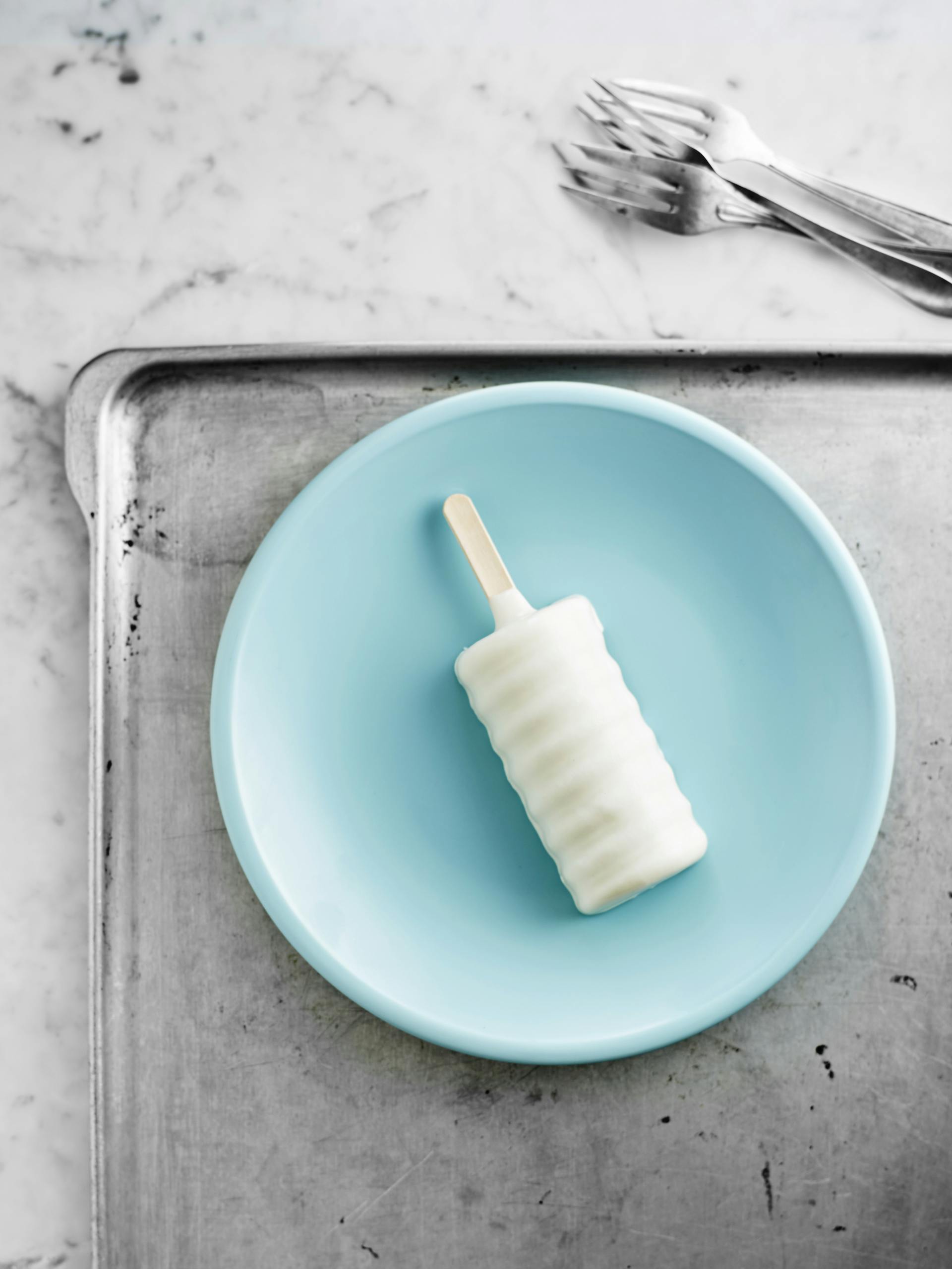 A white popsicle on a blue plate, styled for a refreshing summer snack shot.