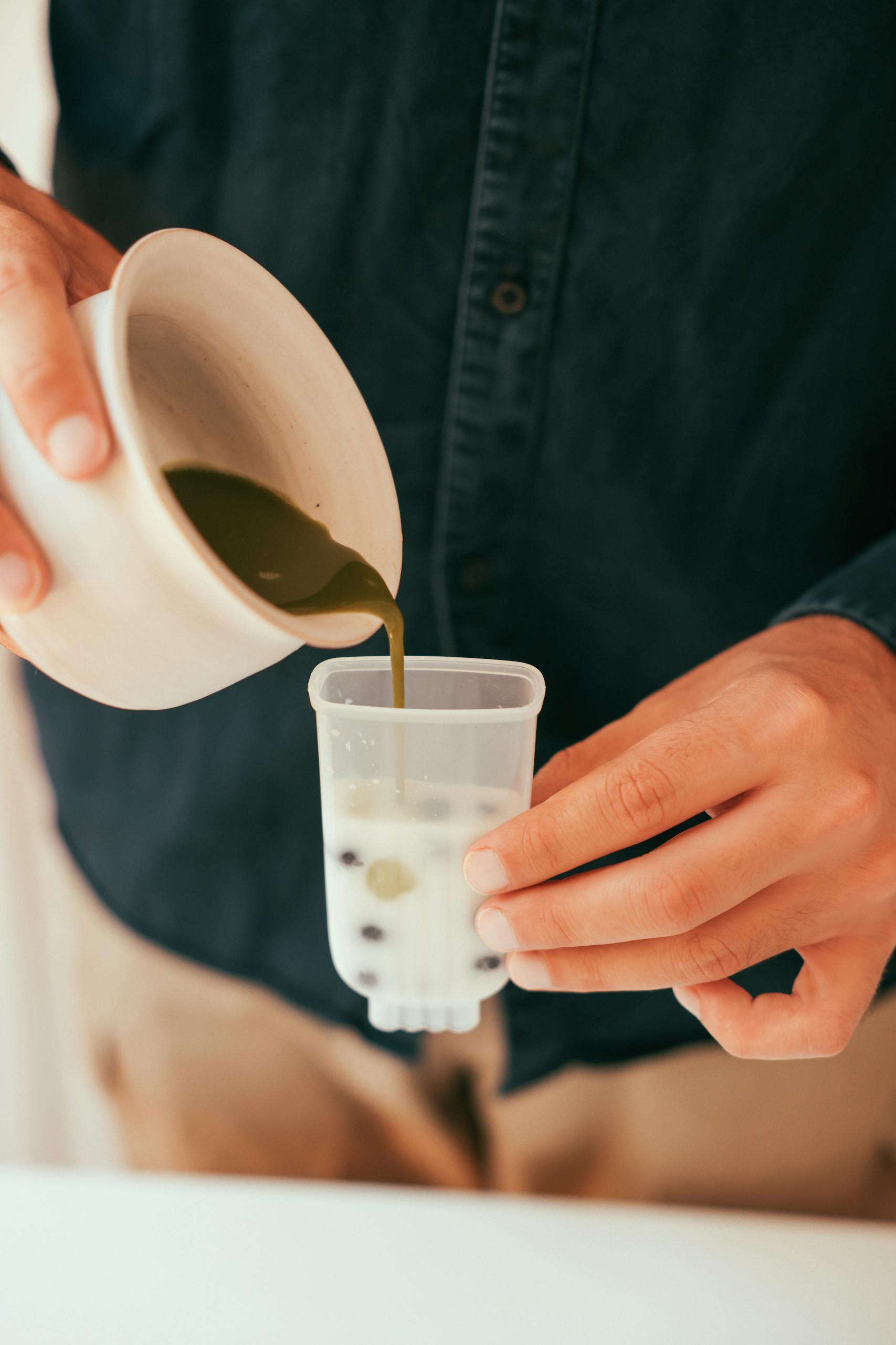 Close-up of hands pouring matcha mixture over blueberries into a popsicle mold.