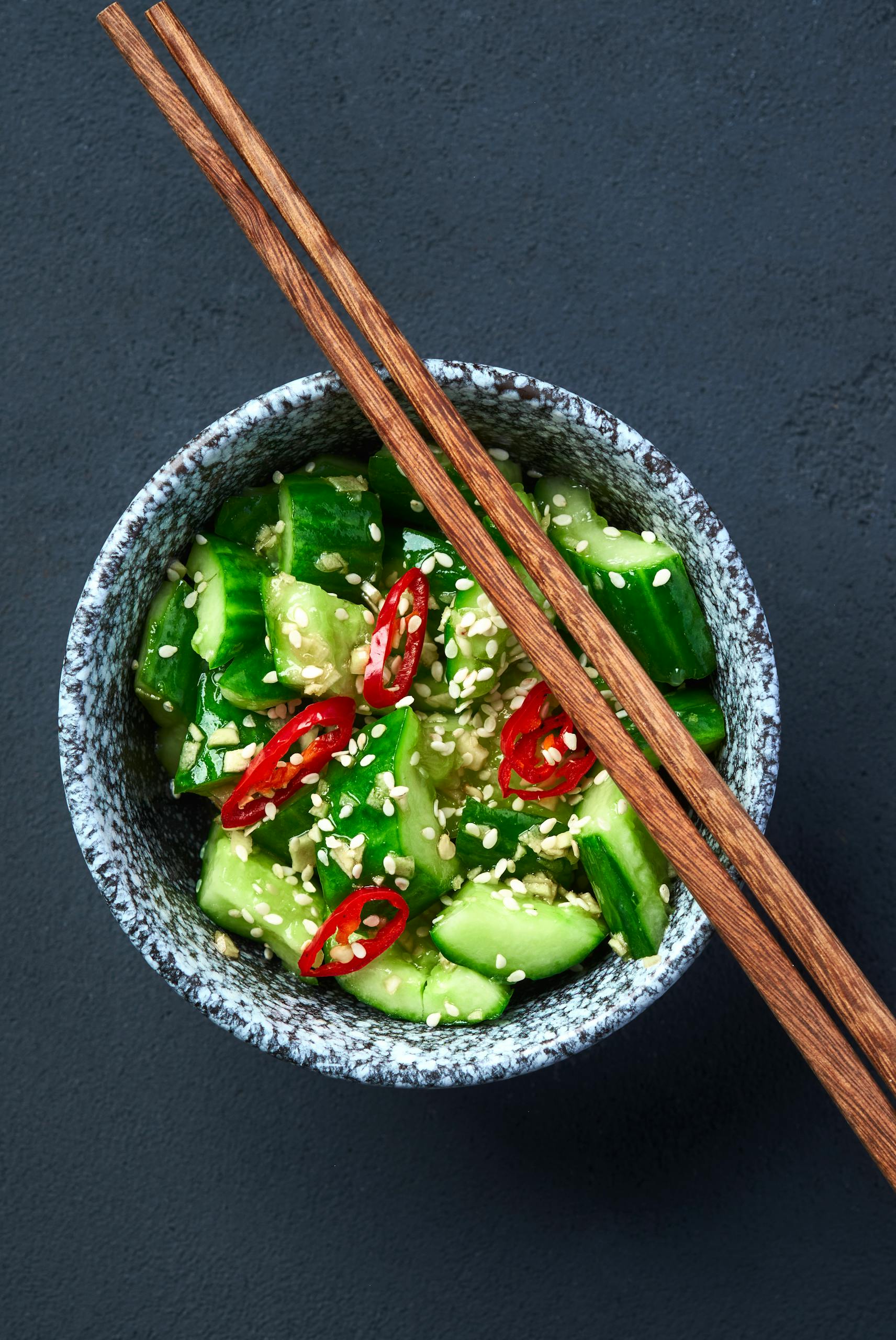 Vibrant cucumber salad garnished with red chili slices and sesame seeds in a bowl.