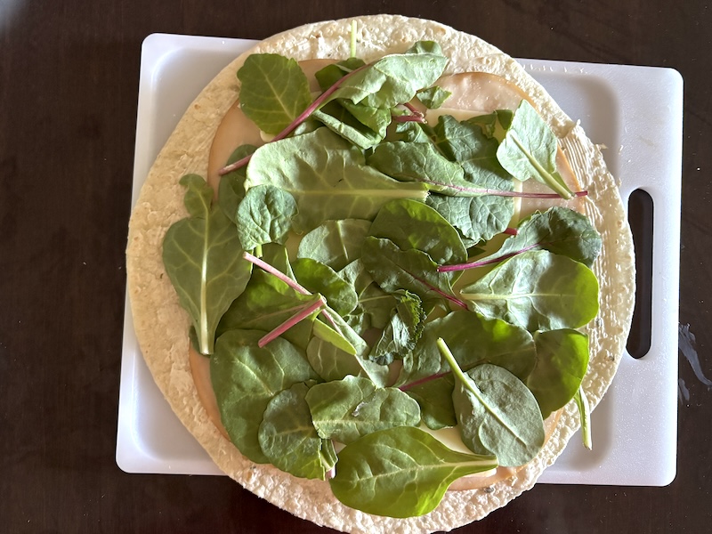 Spinach on top of a tortilla with cream cheese and toppings