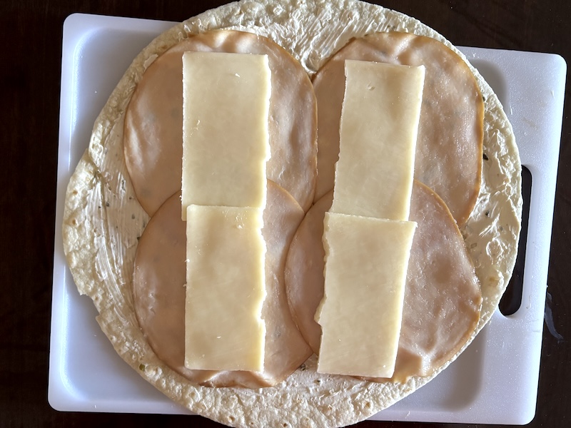 Slices of turkey breast and cheese layered on top of a tortilla with cream cheese