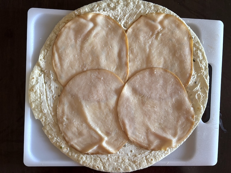 Slices of turkey breast layered on top of a tortilla with cream cheese