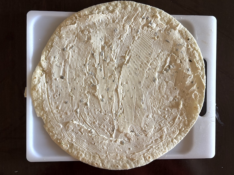 Tortilla on a flat surface with cream cheese layered on top