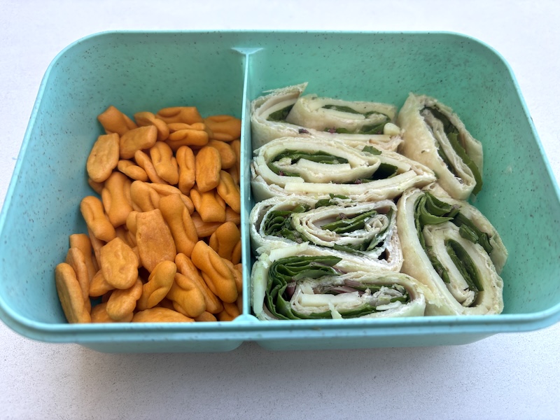 Lunchbox view of spinach turkey cream cheese rollups with cheddar crackers on the side