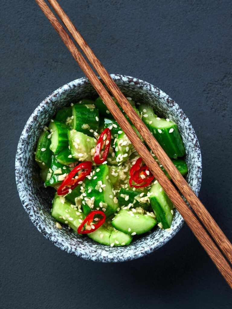 Vibrant cucumber salad garnished with red chili slices and sesame seeds in a bowl.
