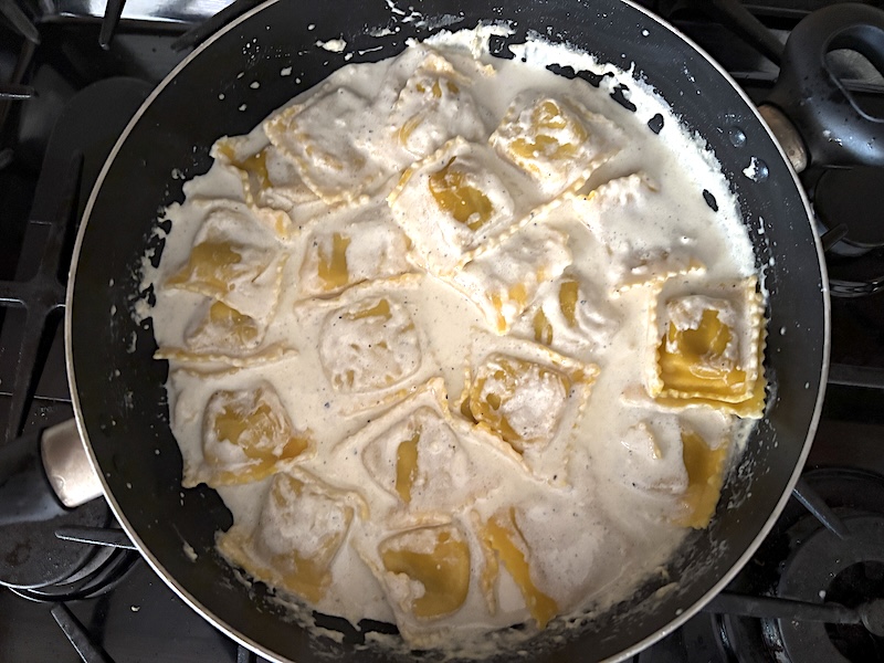 Adding the cooked ravioli to the skillet with the cream sauce