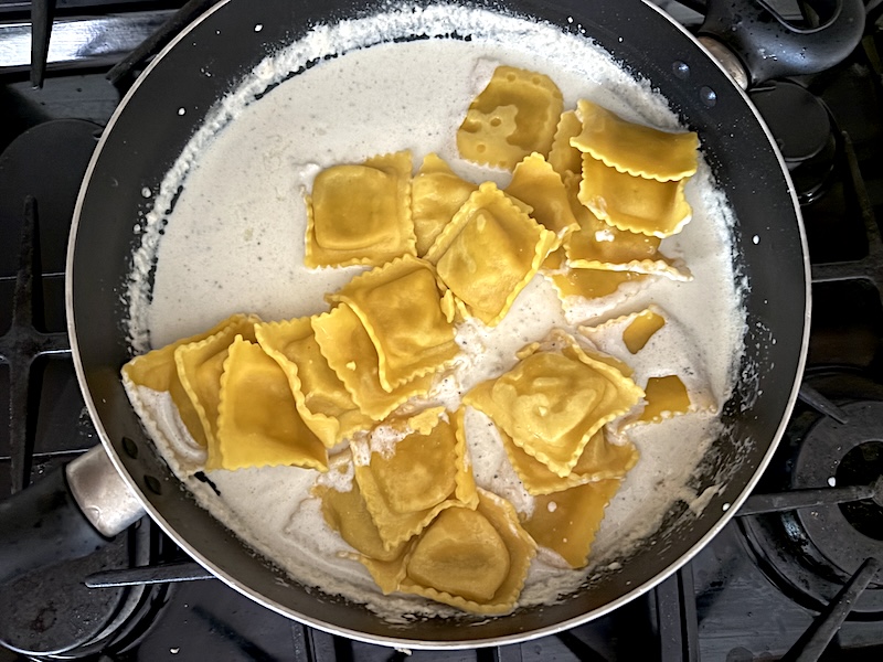 Adding the cooked ravioli to the skillet with the cream sauce