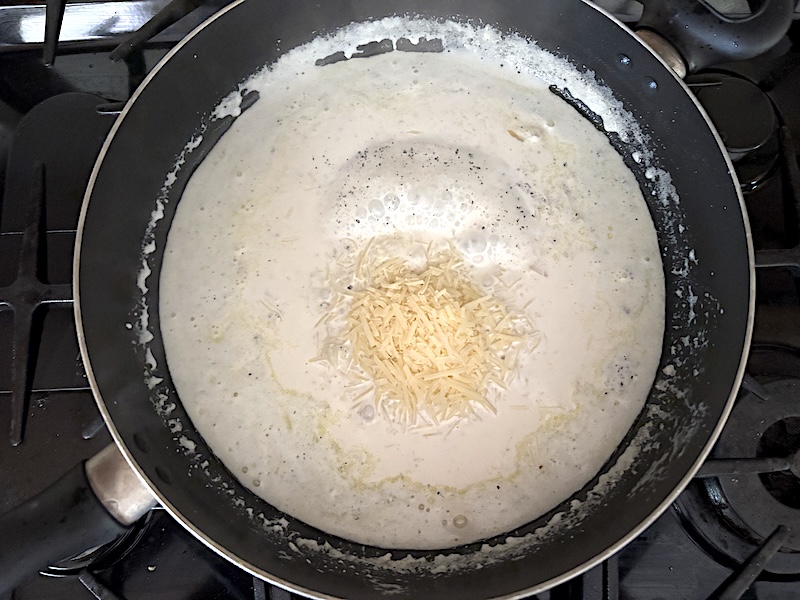 Adding shredded parmesan cheese to the skillet to make the cream sauce