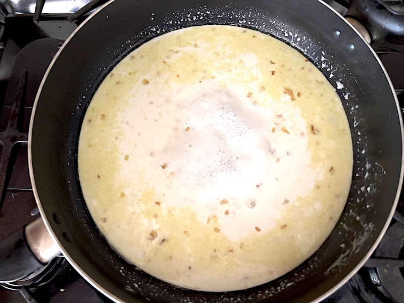 The garlic cream sauce is bubbling gently in a skillet on the stovetop