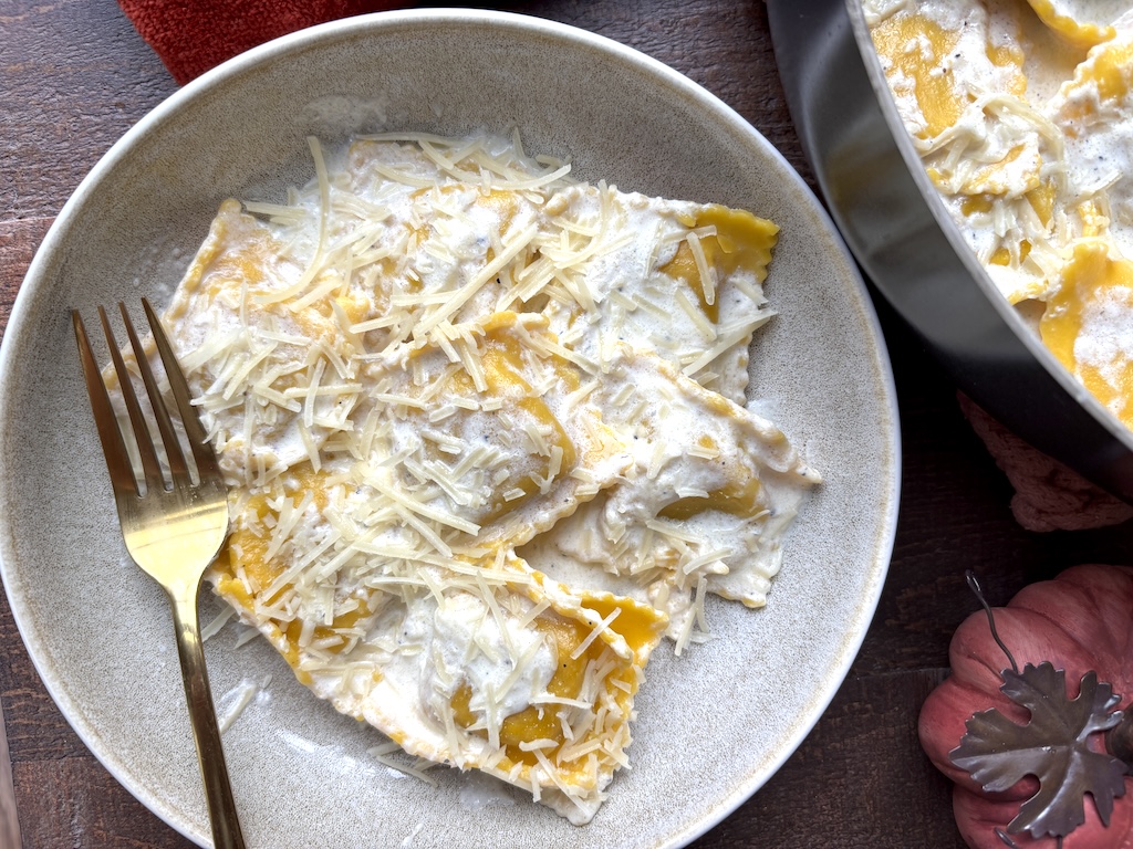 Close-up of a plate of butternut squash ravioli with cream source with a gold fork next to it