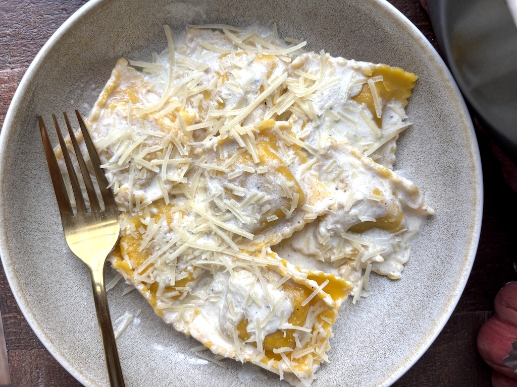 Close-up of a plate of butternut squash ravioli with cream source with a gold fork next to it