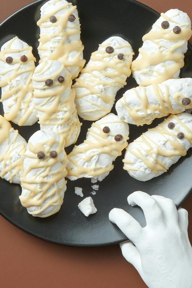 Creepy Halloween-themed sweets arranged with toy spiders and a fake hand. Perfect for festive occasions.