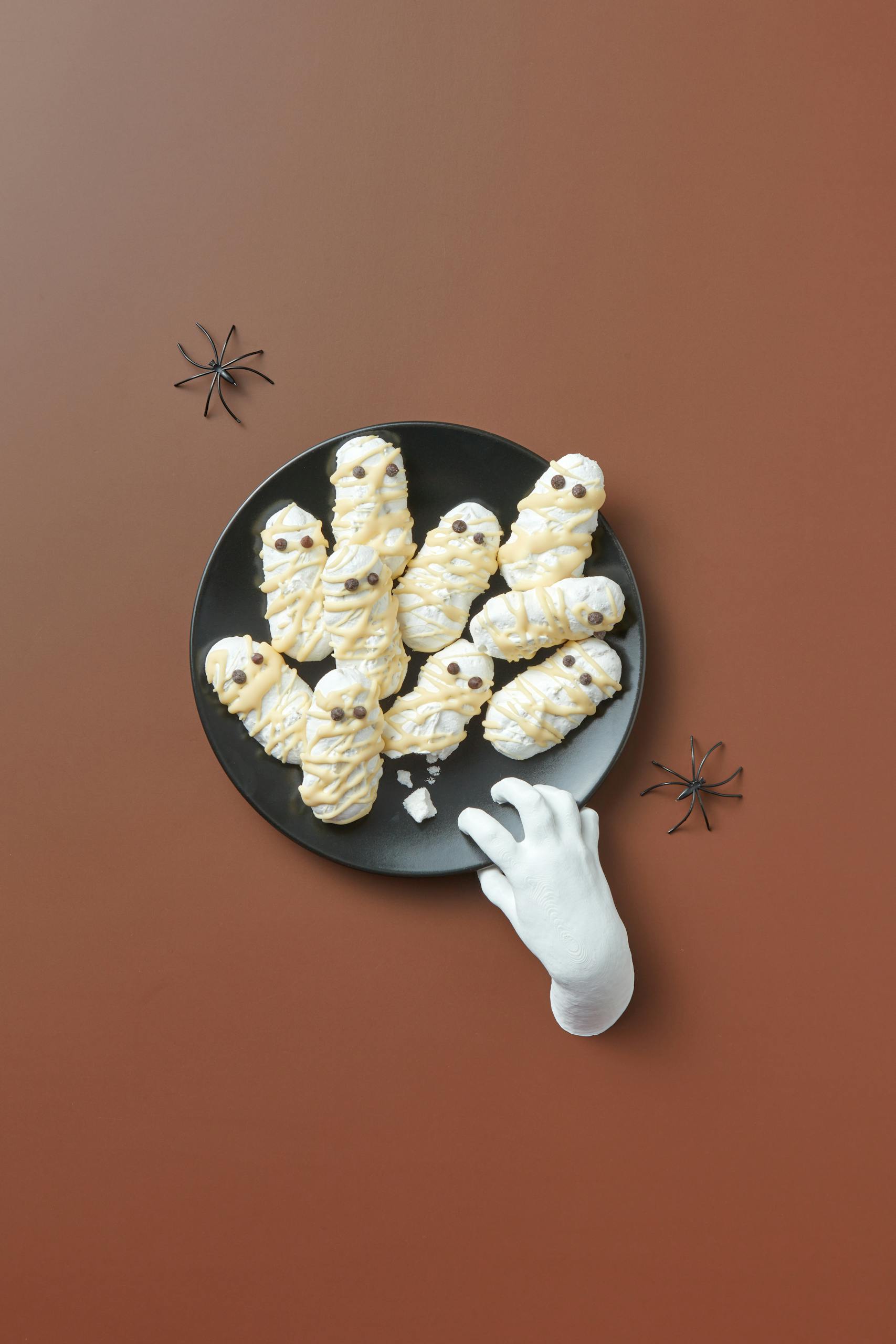 Creepy Halloween-themed sweets arranged with toy spiders and a fake hand. Perfect for festive occasions.