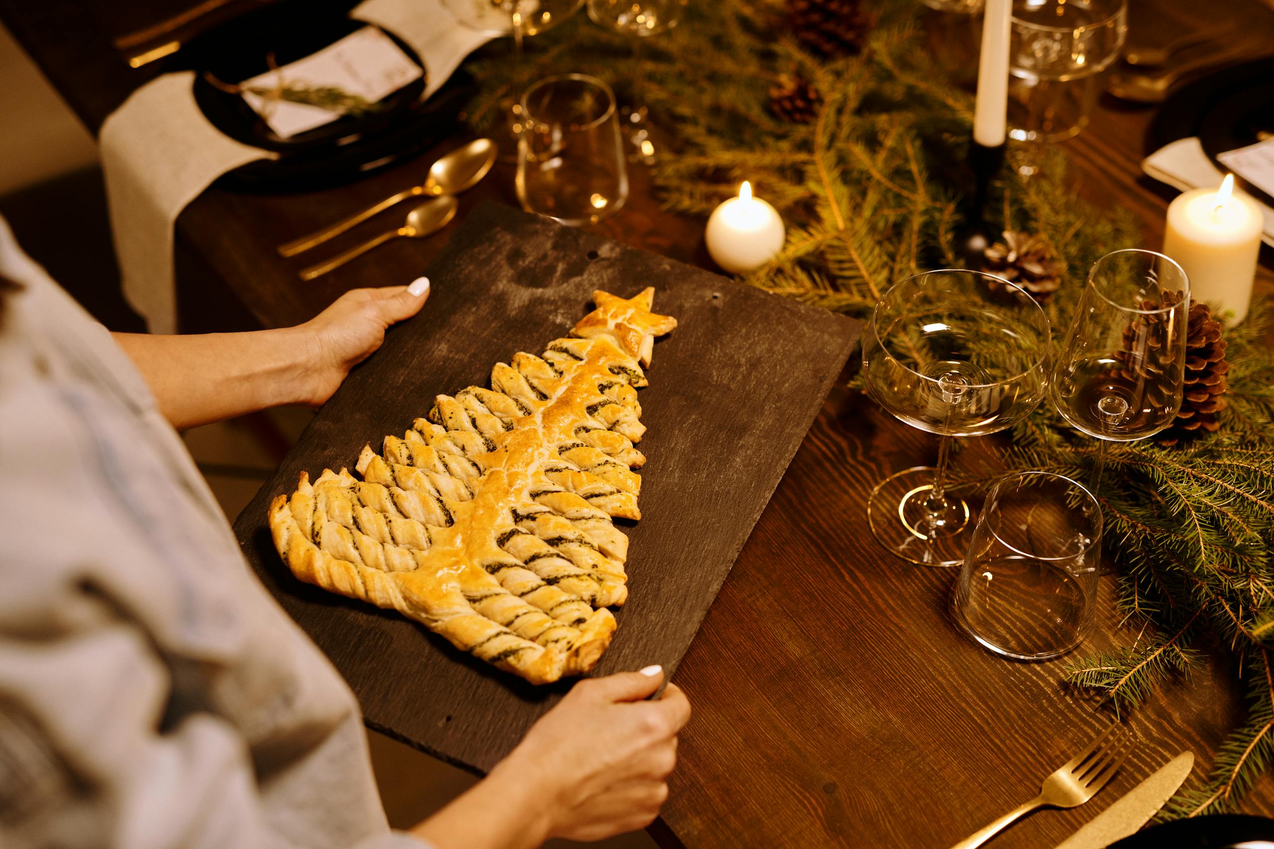 A Christmas-themed pastry shaped like a tree on a decorated dining table with candles.