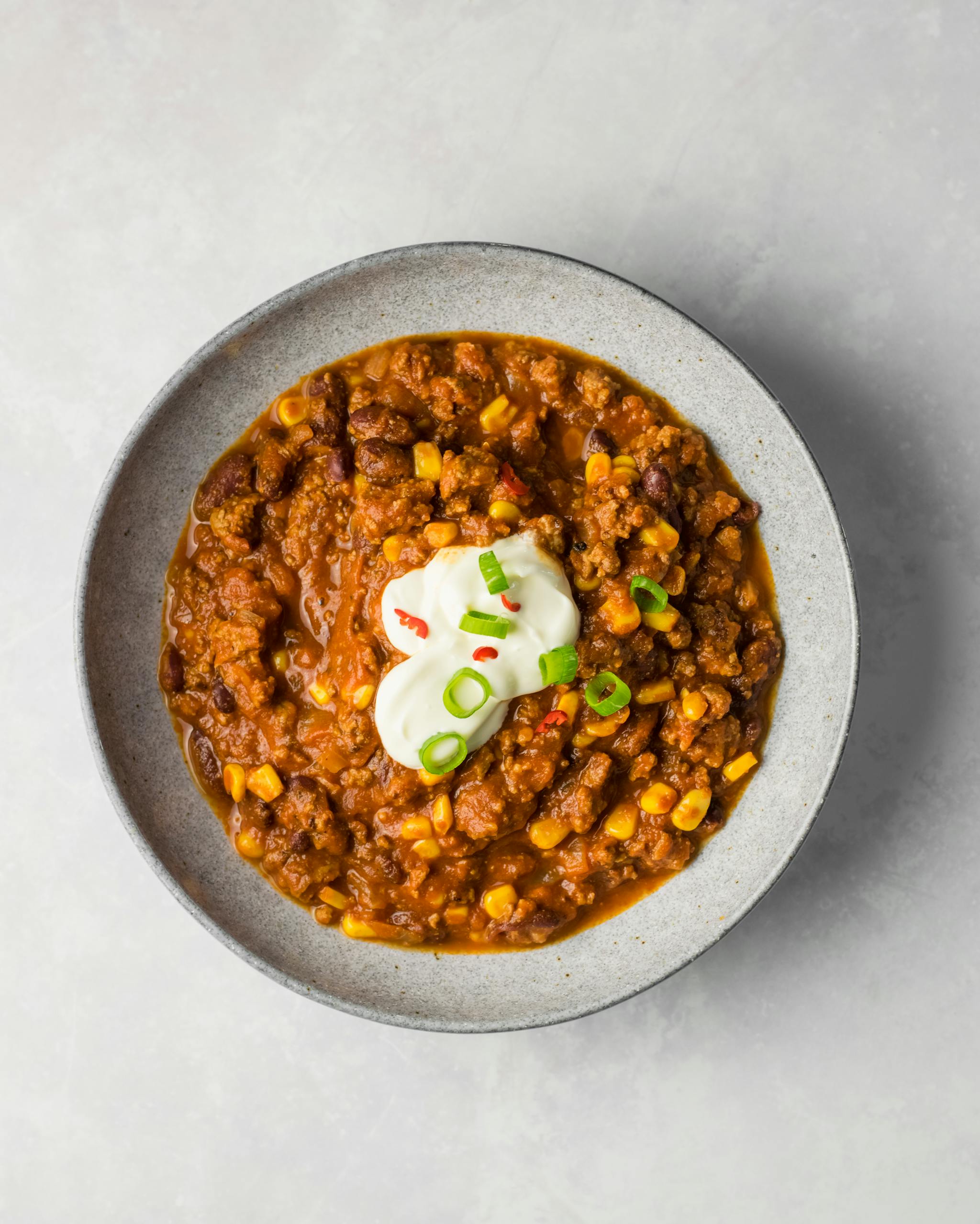 Delicious chili con carne with beans, corn, and sour cream garnish, perfect for dinner.