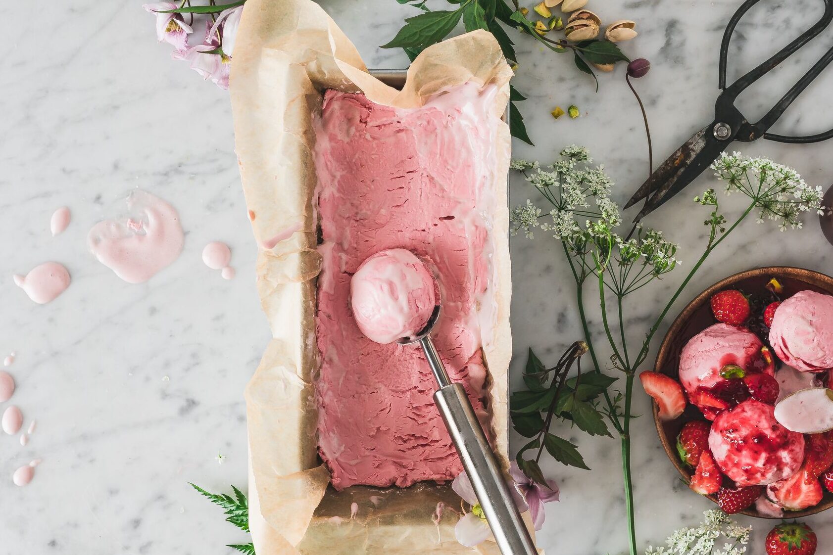 Top-down view of homemade strawberry ice cream with fresh berries and decor on a marble surface.
