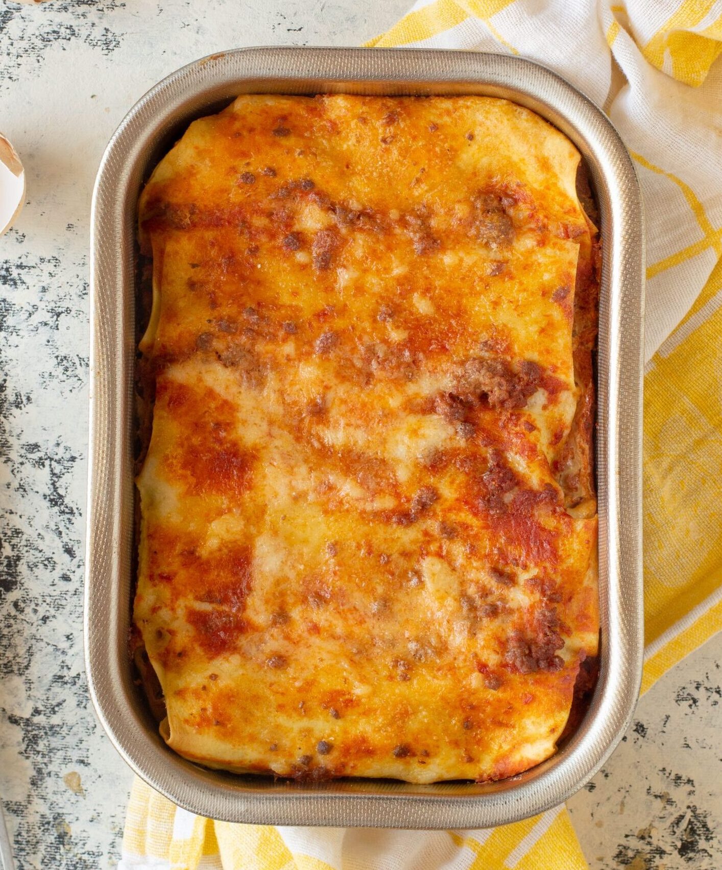 Delicious homemade lasagna in baking dish surrounded by eggs and kitchen utensils.